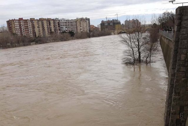 High-angle view of the flooded Ebro River in Zaragoza with apartment buildings and submerged trees along the banks.