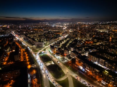 Aerial drone photograph of a city at night with illuminated streets, buildings, and vehicle headlights on a highway