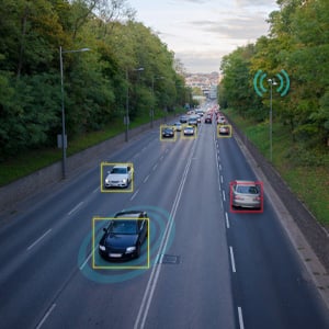 High-angle view of cars on a multi-lane city road with digital tracking boxes and signal graphics overlaying the traffic