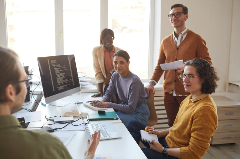 A group of developers sitting around a table, listening to their team leader.