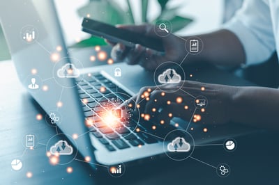 Close-up of hands typing on a laptop and holding a smartphone with overlaid digital cloud and data network icons