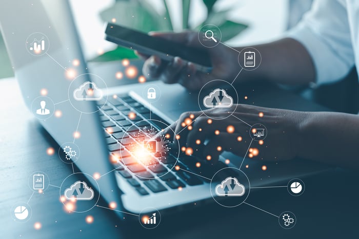 Close-up of hands typing on a laptop and holding a smartphone with overlaid digital cloud and data network icons