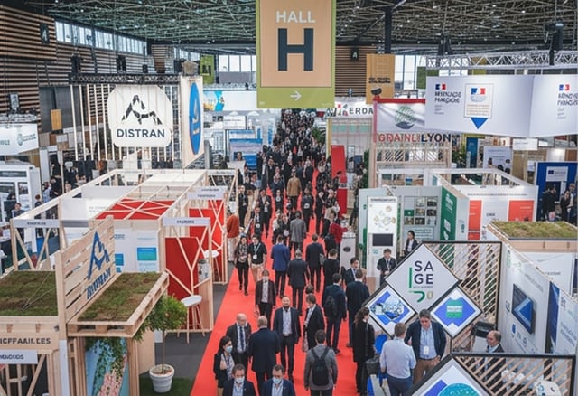 Crowded exhibition hall at Pollutec in Lyon with visitors walking along a red carpet between various company booths