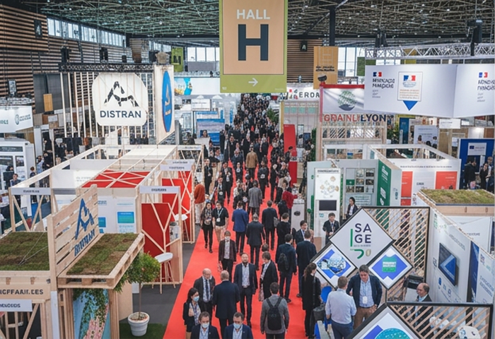 Crowded exhibition hall at Pollutec in Lyon with visitors walking along a red carpet between various company booths