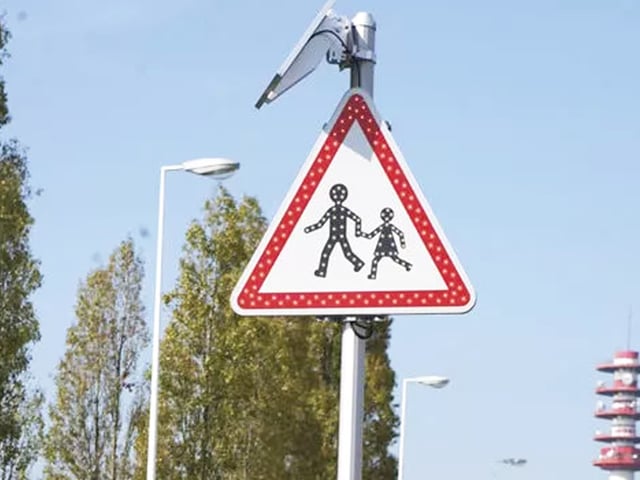 A LACROIX solar-powered LED pedestrian crossing sign on a metal pole against a blue sky.