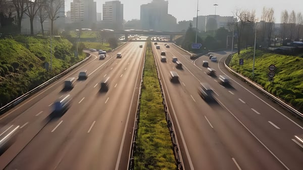 High-angle view of blurred cars traveling on a multi-lane city highway with a skyline and overpass in the distance.