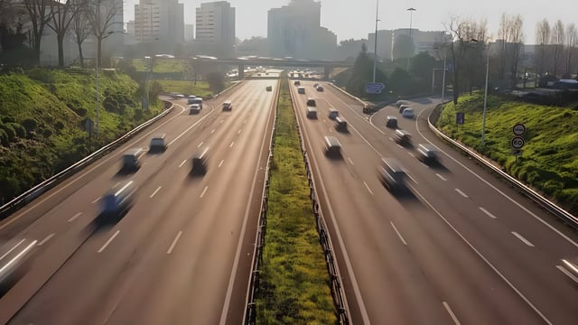 High-angle view of blurred cars traveling on a multi-lane city highway with a skyline and overpass in the distance.