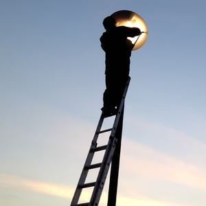 A person on a ladder fixing a smart luminaire that is connected to a control cabinet