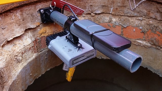Flood monitoring IoT sensors and equipment mounted on a PVC pipe inside a brick manhole.