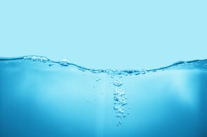 Close-up of a clean blue water surface wave with rising air bubbles against a light blue background