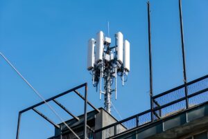Cellular base station with white panel antennas mounted on a metal rooftop structure against a clear blue sky.