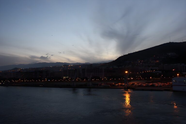 Distant view of Santa Cruz de Tenerife at dusk with street lights reflecting on the harbor water below dark hills.