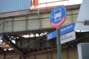 A New York City B3 bus stop sign for Bergen Beach at Avenue U and McDonald Avenue under an elevated train track.