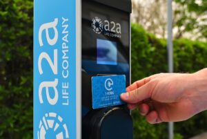 A hand taps an E-moving RFID card against an A2A branded electric vehicle charging station.