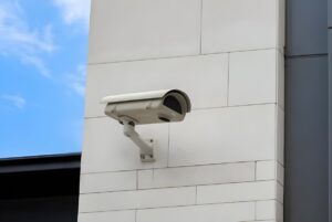 White bullet-style security camera mounted on a light-colored stone building facade against a blue sky.