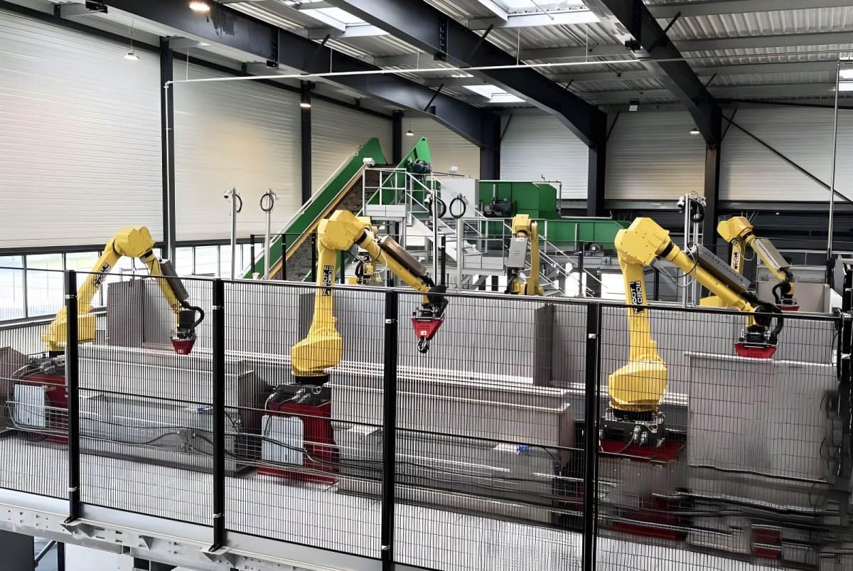 Yellow Waste Robotics arms sorting materials over a conveyor system inside a large industrial waste management facility.