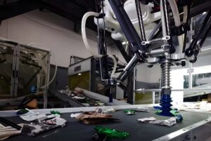 An AMP Robotics high-speed delta robot sorts recyclable materials on a conveyor belt in a waste management facility.