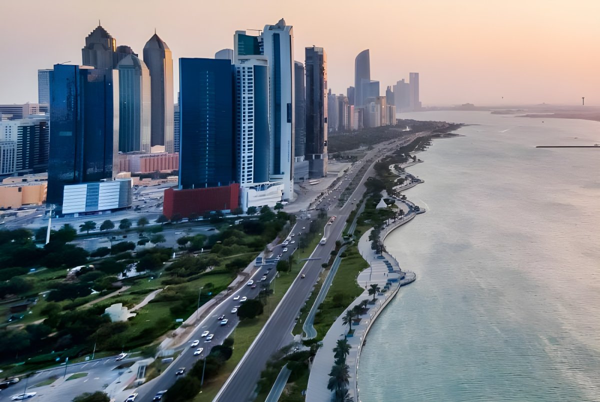 Aerial view of the Abu Dhabi Corniche skyline and waterfront highway at dusk.
