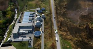 Aerial drone view of a water treatment plant with circular tanks and rectangular basins situated next to a rural road.