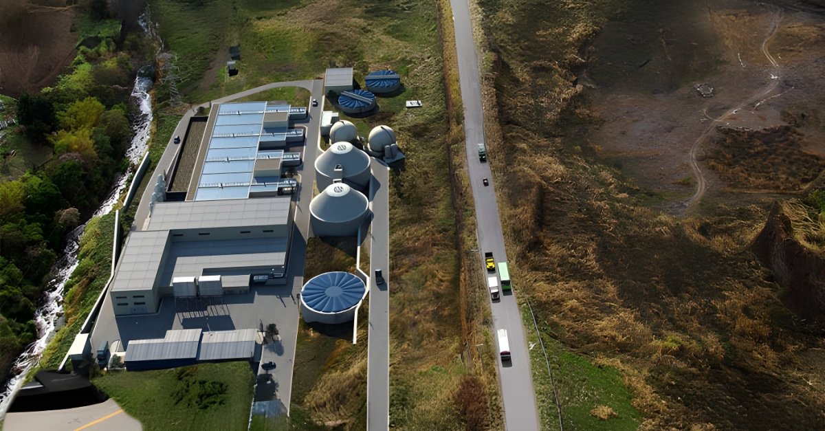 Aerial drone view of a water treatment plant with circular tanks and rectangular basins situated next to a rural road.