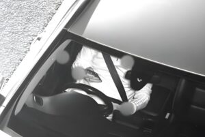 Black and white Acusensus camera view of a driver holding a mobile phone behind a steering wheel.