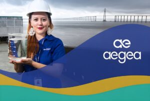 Aegea worker in a hard hat holding a water beaker near a bridge, with the Aegea logo in the foreground.
