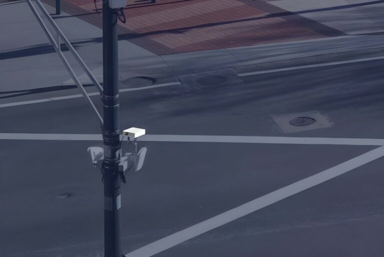An Aeva LiDAR sensor and traffic cameras mounted on a utility pole overlooking a city intersection.