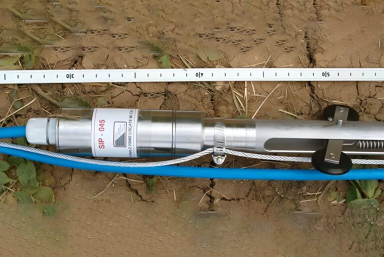 An Agisco SIP-045 geotechnical sensor probe with blue cabling and a measuring tape on dry, cracked earth.