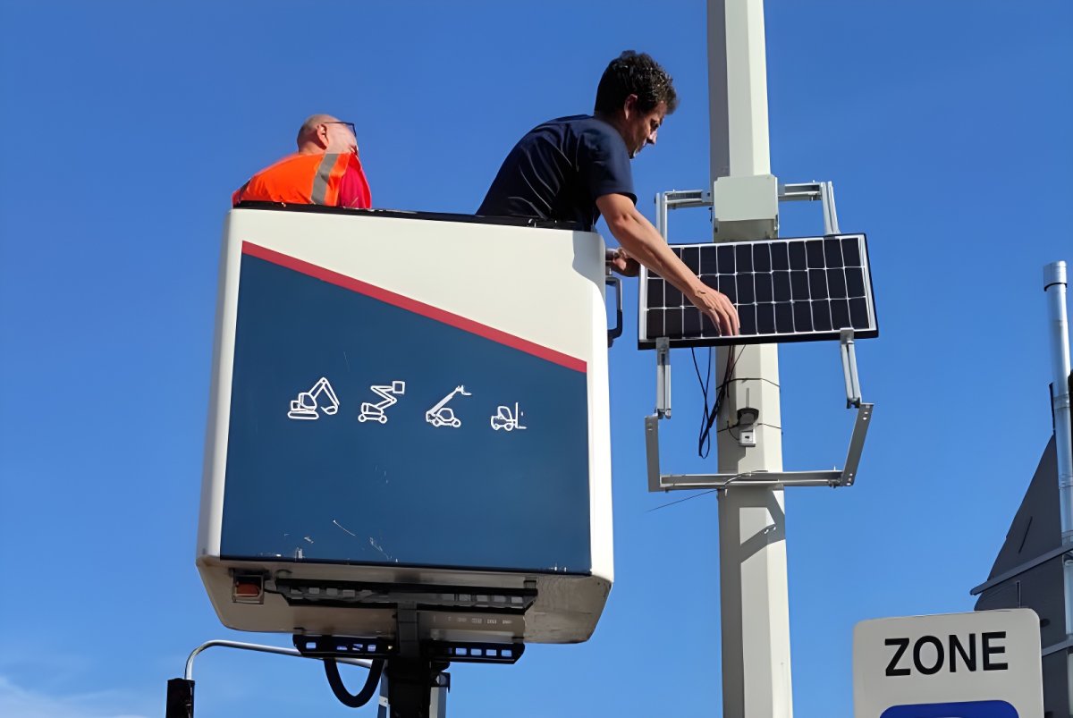 Technicians in a cherry picker bucket install an Airly air quality sensor and solar panel onto a street pole.