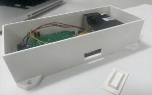 Internal view of a SACAQM air quality sensor showing a green circuit board and wiring inside a white 3D-printed enclosure.