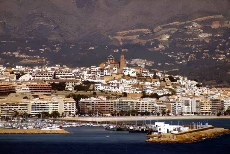 Coastal view of Altea, Spain, featuring the hilltop church, white buildings, and a harbor against a mountain backdrop.