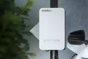 A white Ambibox bidirectional electric vehicle charger mounted on a wall next to a parked car.