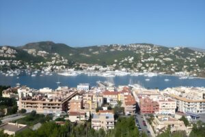 Elevated view of Port d'Andratx featuring a harbor filled with boats, coastal buildings, and forested hills in Mallorca.