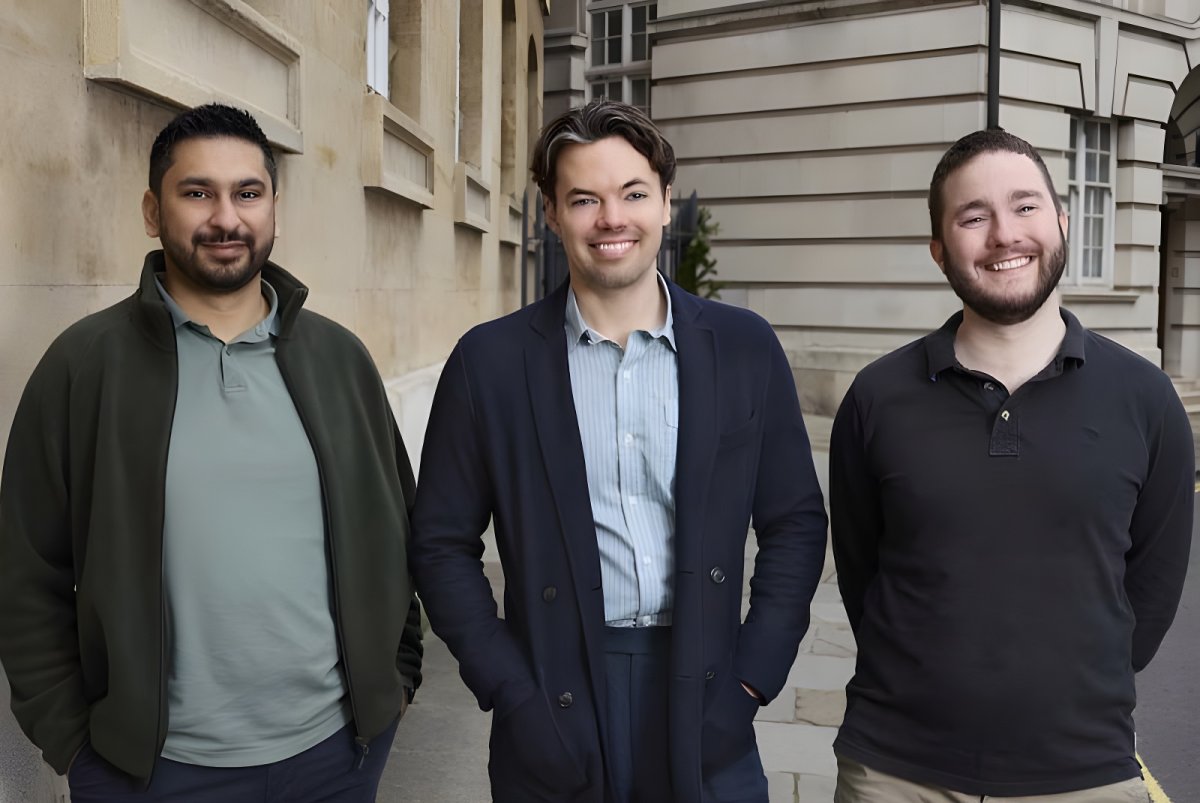 Three men standing outdoors on a sidewalk in front of stone buildings.