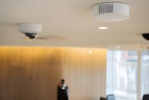 An Axis Communications environmental sensor and a dome security camera mounted on an indoor ceiling.