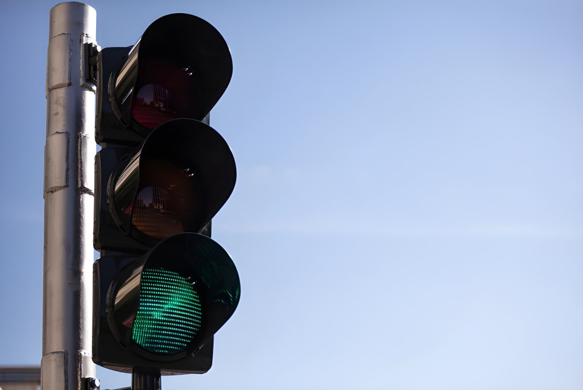 Close-up of a vertical three-lens traffic light with the green signal illuminated against a clear blue sky.