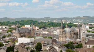 Panoramic aerial view of the Aachen city skyline featuring the Aachen Cathedral and Town Hall under a blue sky.