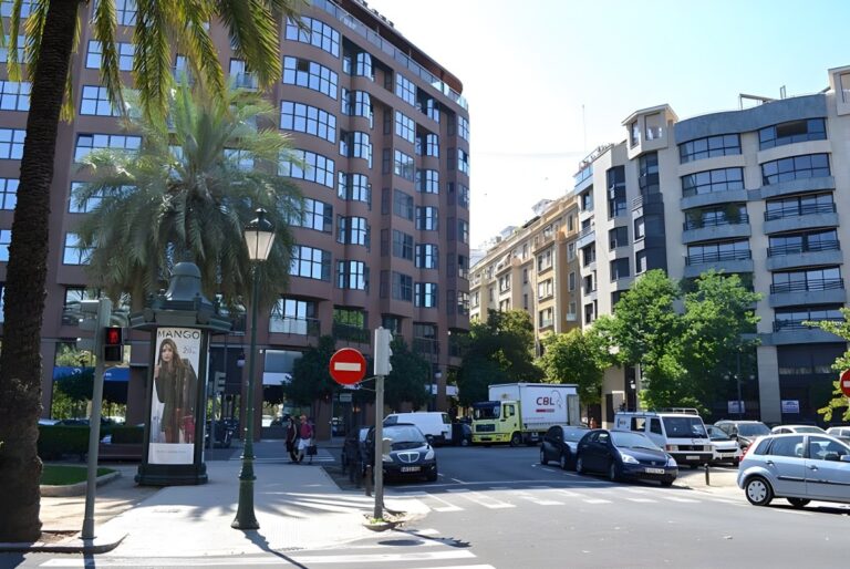 Street view of a Burriana city intersection with multi-story apartment buildings, palm trees, and parked cars.