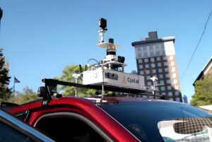 CYVL AI-LiDAR mapping sensors and cameras mounted on the roof rack of a red vehicle in a city.