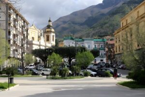 Street level view of a public square and parking lot in Castellammare di Stabia with mountains in the background.