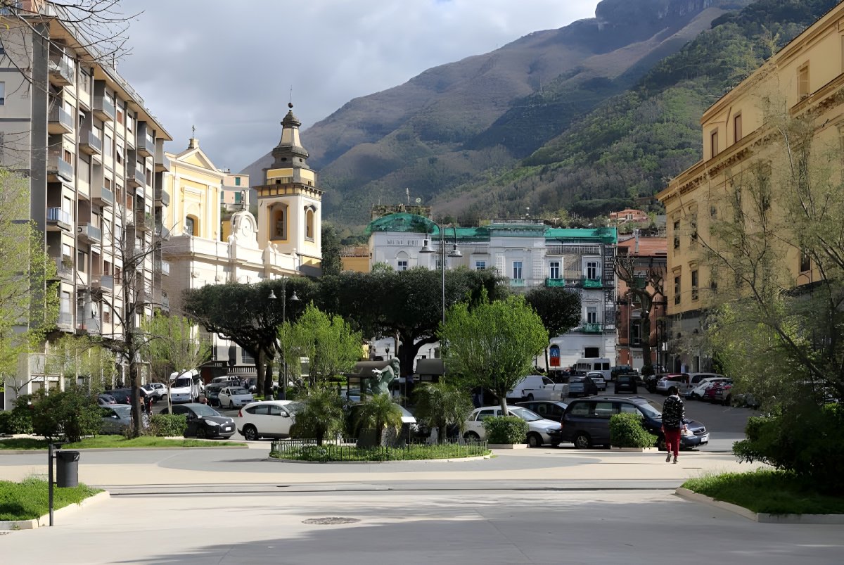 Street level view of a public square and parking lot in Castellammare di Stabia with mountains in the background.
