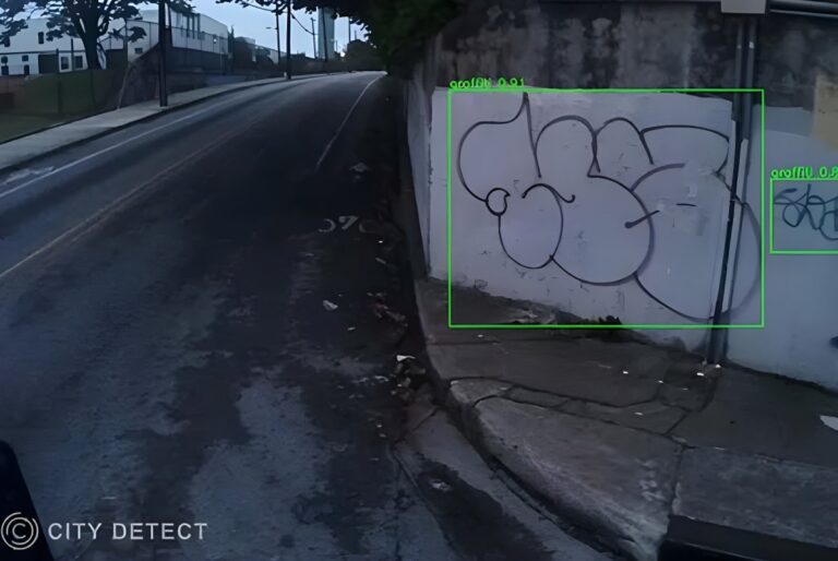 City Detect AI software identifies graffiti on a concrete wall with green bounding boxes along a city street.