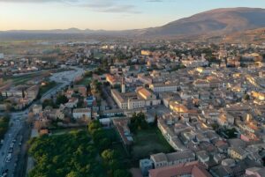 Aerial drone view of the Foligno city center and surrounding valley at sunset with mountains in the background.