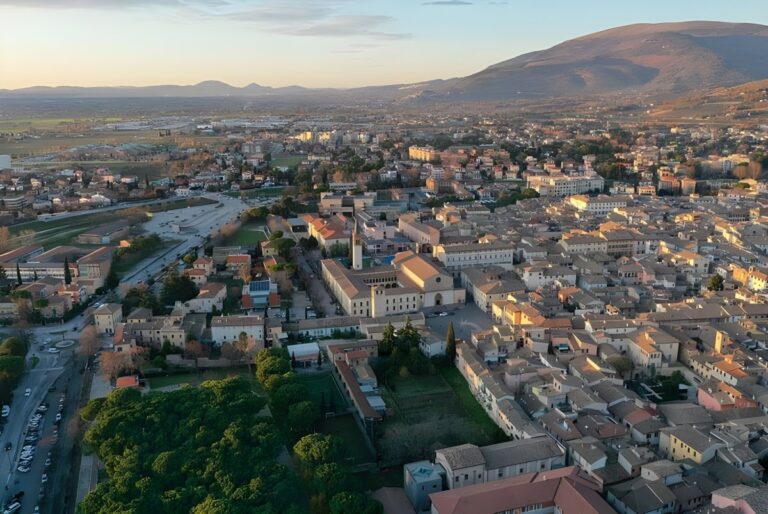 Aerial drone view of the Foligno city center and surrounding valley at sunset with mountains in the background.