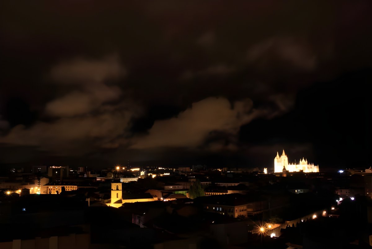 Nighttime aerial view of the León skyline featuring the illuminated cathedral and glowing street lights under a cloudy sky.