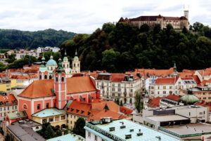 High-angle view of the Ljubljana skyline featuring the Franciscan Church of the Annunciation and Ljubljana Castle on a hill.