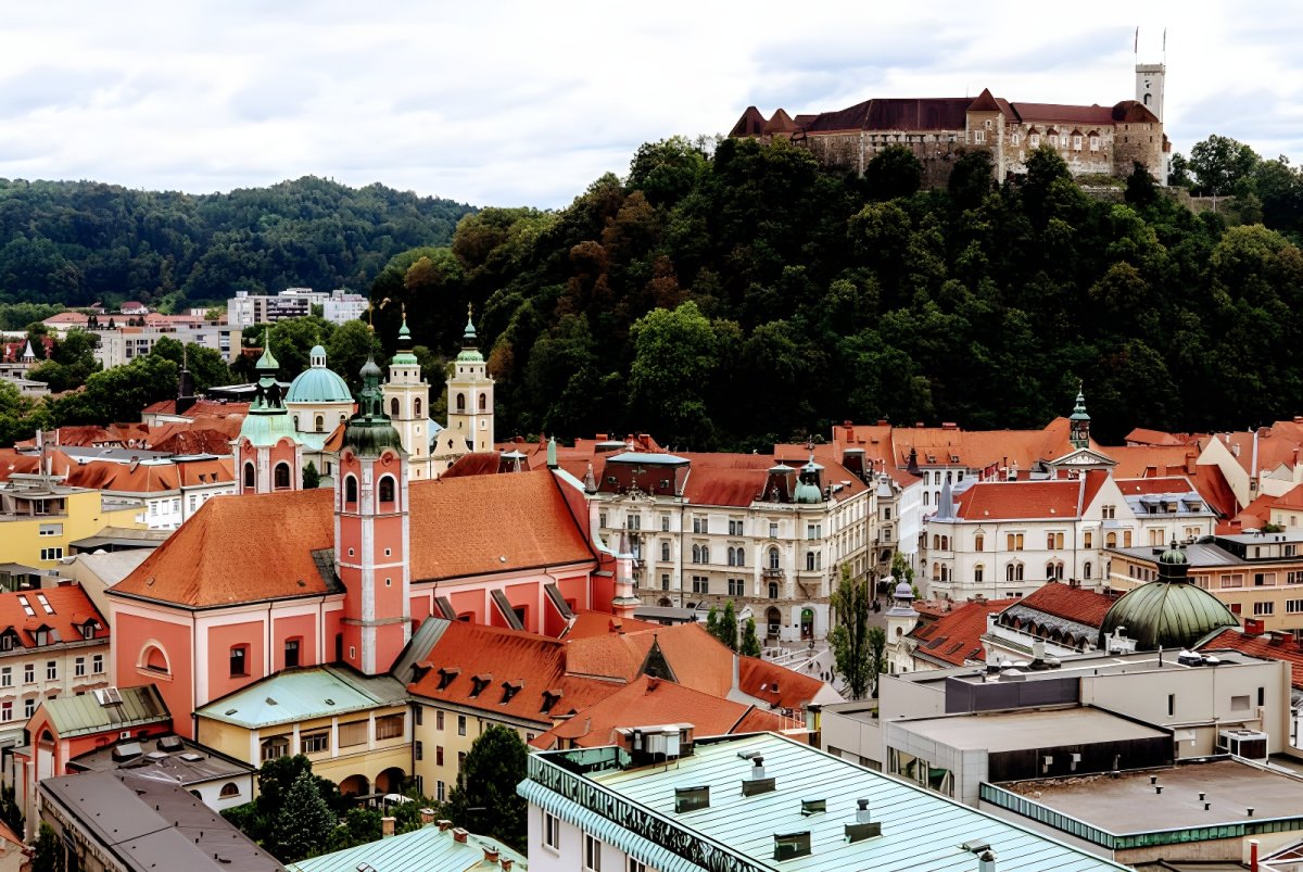 High-angle view of the Ljubljana skyline featuring the Franciscan Church of the Annunciation and Ljubljana Castle on a hill.