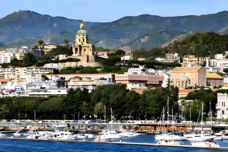Panoramic view of the Messina harbor and skyline featuring the Sacrario di Cristo Re against a backdrop of green hills.