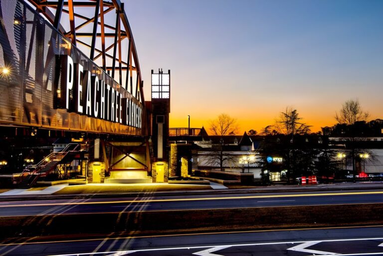 Illuminated Peachtree Corners pedestrian bridge over a multi-lane road at sunset.
