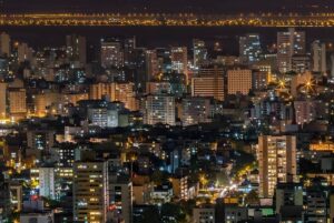 Nighttime aerial view of the Porto Alegre skyline featuring illuminated high-rise buildings and glowing street lights.